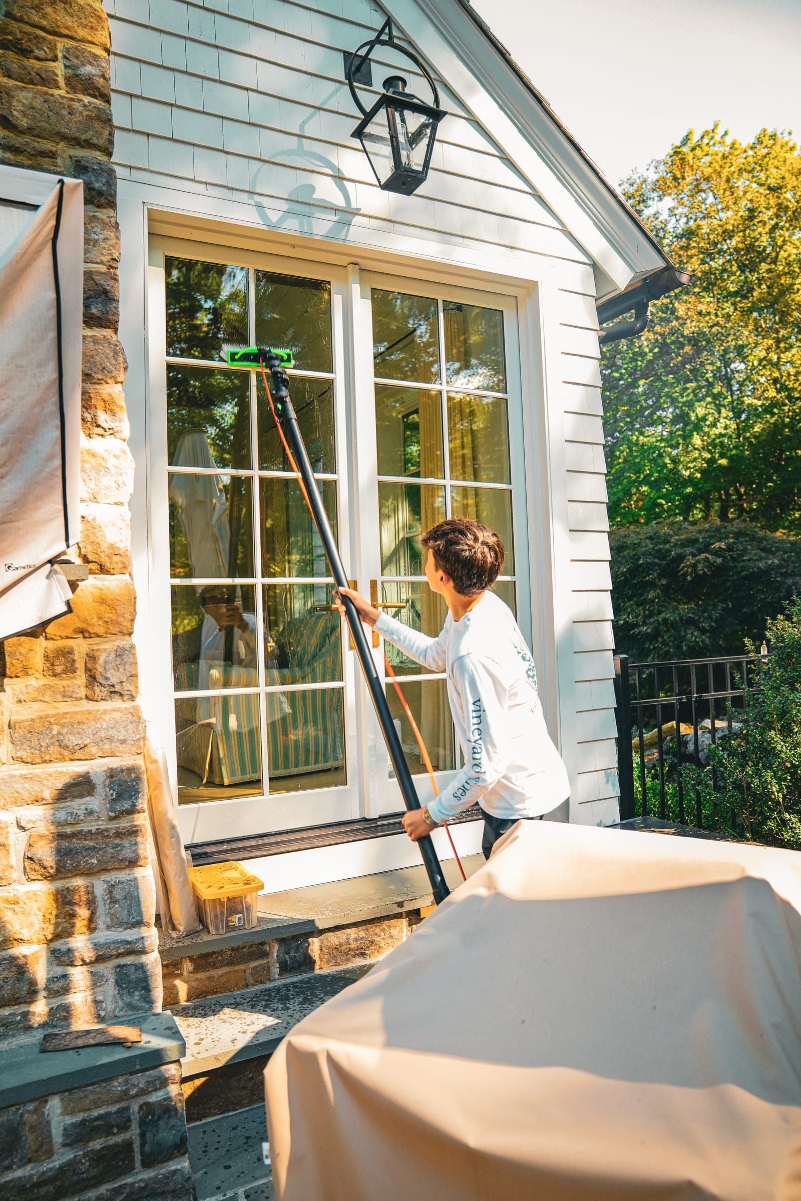 Cleaner washing a tall window above a covered patio table