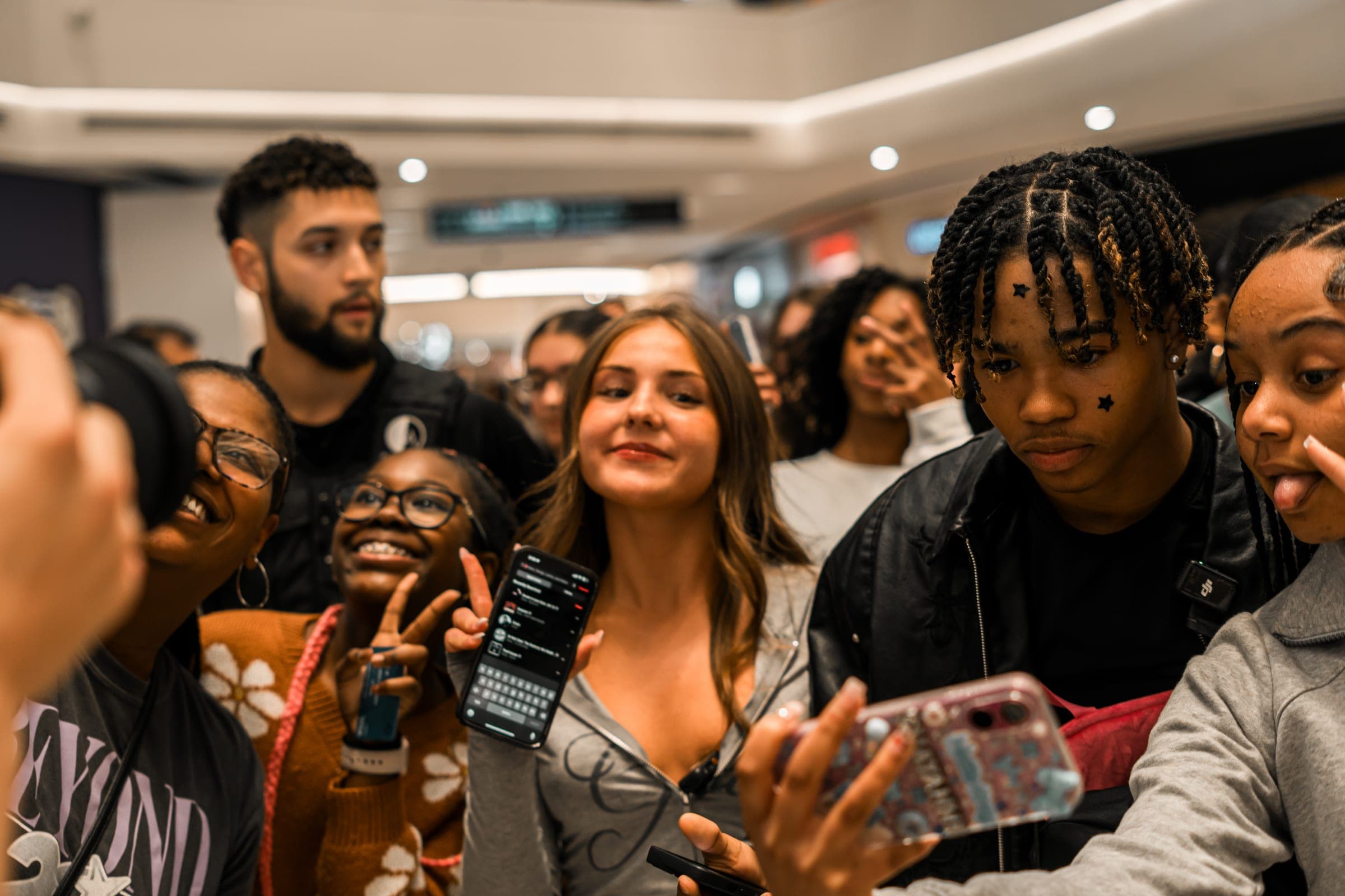 Fans holding up phones and smiling around a creator at a mall meet-up